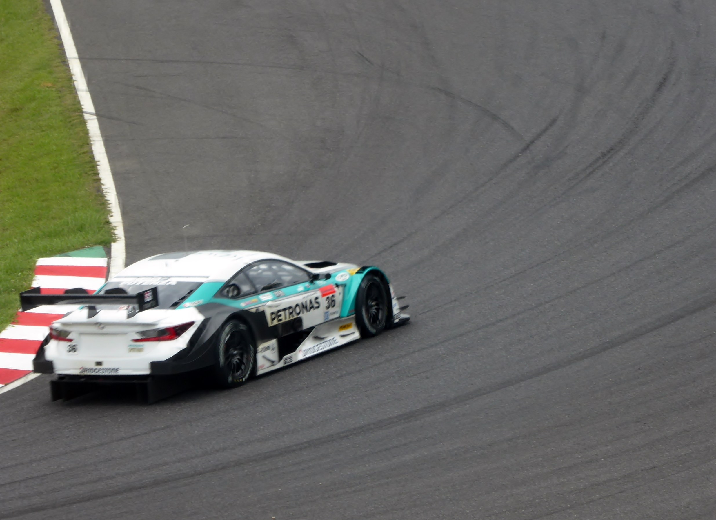 Ein Mercedes-AMG GT3 Rennwagen auf einer Rennstrecke mit Text auf der Karosserie und Gras links daneben.