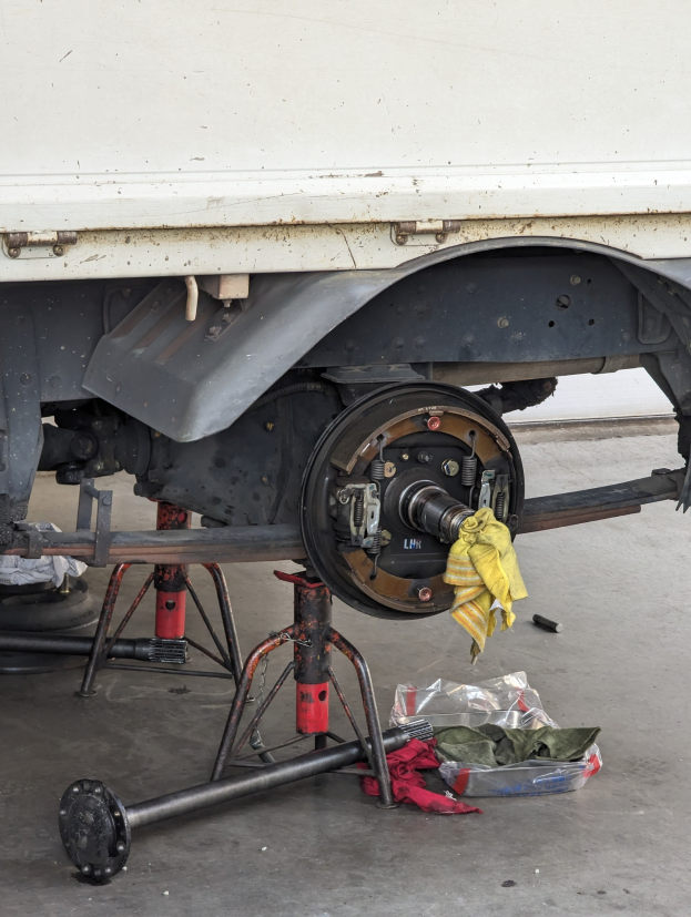 Ein gelbes Tuch liegt auf einem Lastwagen, der in einer Garage geparkt ist, mit Werkzeugen und Gegenständen, die vor ihm auf dem Boden verstreut sind.