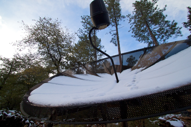 Eine Schüsselantenne mit Schnee darauf, mit ein paar Bäumen und einem klaren Himmel im Hintergrund.