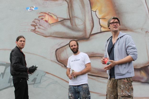 Leute stehen und halten Farbsprühflaschen vor einer Wand mit Graffiti.