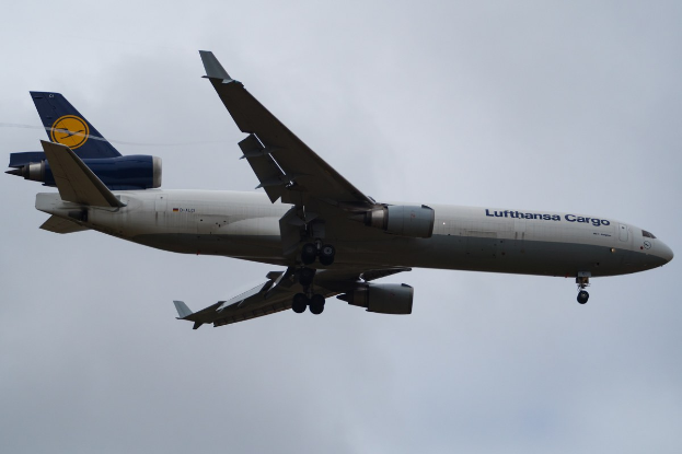 Lufthansa Cargo Boeing 777-300ER im Flug mit sichtbarem Text auf dem Rumpf, ausgefahrenen Tragfl"achen und aktivierten Triebwerken gegen einen teilweise bew"olkten Himmel.