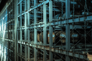 Großes Lager mit zahlreichen Fässern, die in ordentlichen Metallregalen gestapelt und durch Stangen und Ketten verbunden sind.