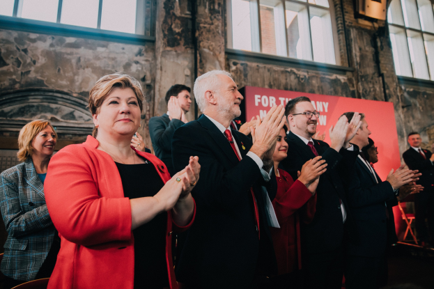 Eine Gruppe von Menschen klatscht und feiert vor einer Menge, mit einem Banner mit Text im Hintergrund.